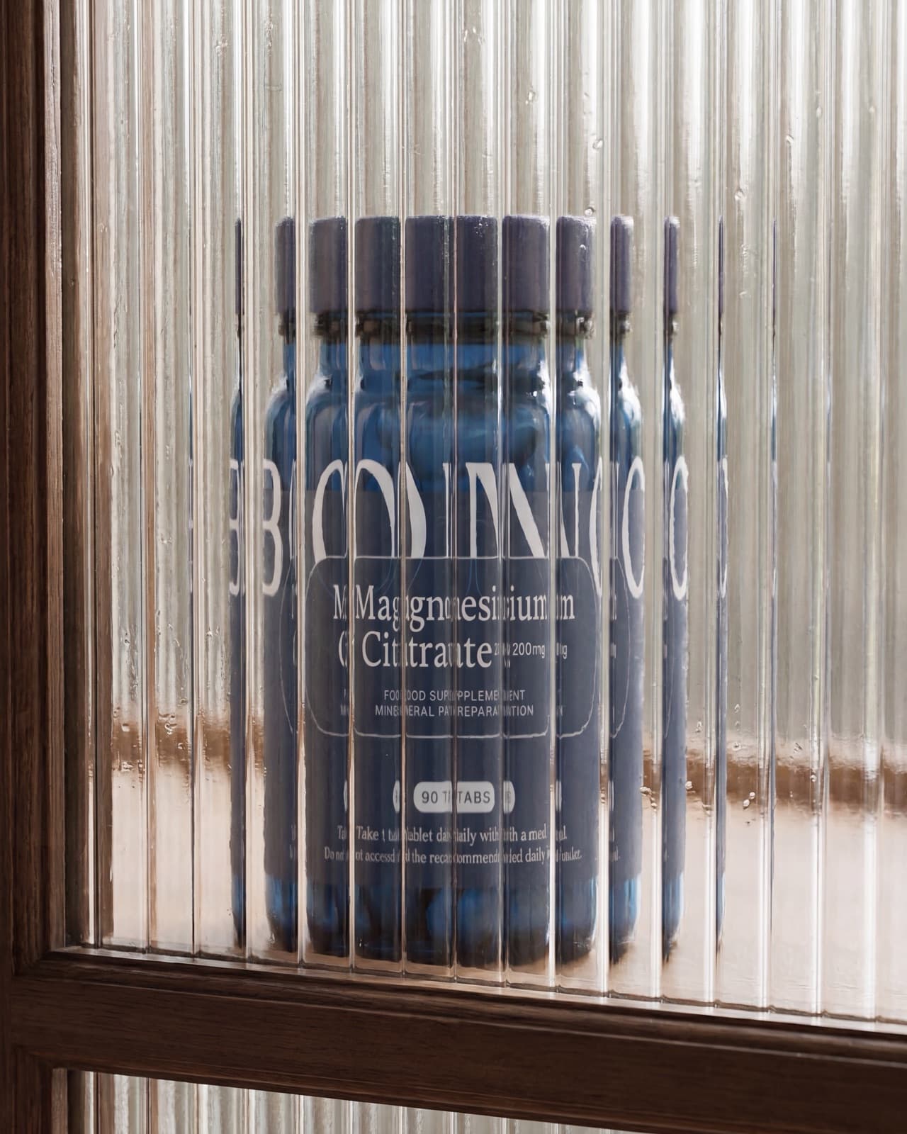 Um frasco de BONO Supplements Citrato de magnésio atrás de vidro canelado